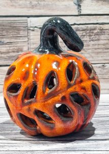 Ażurowy lampion z ceramicznej dyni w kolorze pomarańczowym z wycięciami na świeczkę, wykonany na warsztatach w Warszawie.