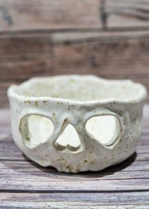 Kremowa nakrapiana miseczka ceramiczna z wyciętym motywem czaszki na tealight, ulepiona na warsztatach jesiennych.