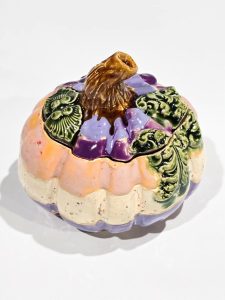 Zamknięta pastelowa szkatułka ceramiczna w kształcie dyni z fioletowo-różowym szkliwem i dekoracyjnymi zielonymi liśćmi.
