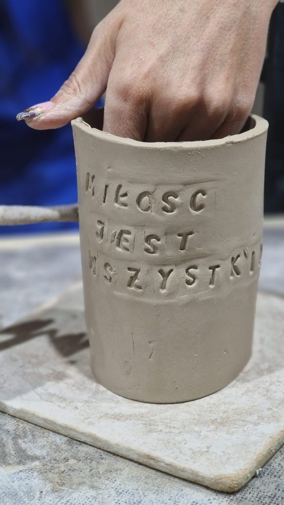 Uczestnik warsztatów wygładzający gliniany kubek z odciśniętym stemplem napisem Miłość jest wszystkim.