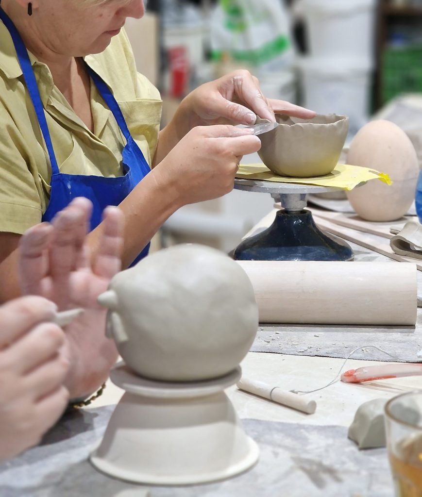 Uczestniczka warsztatów ceramicznych wygładzająca brzeg ulepionej miseczki na toczku modelarskim w pracowni.