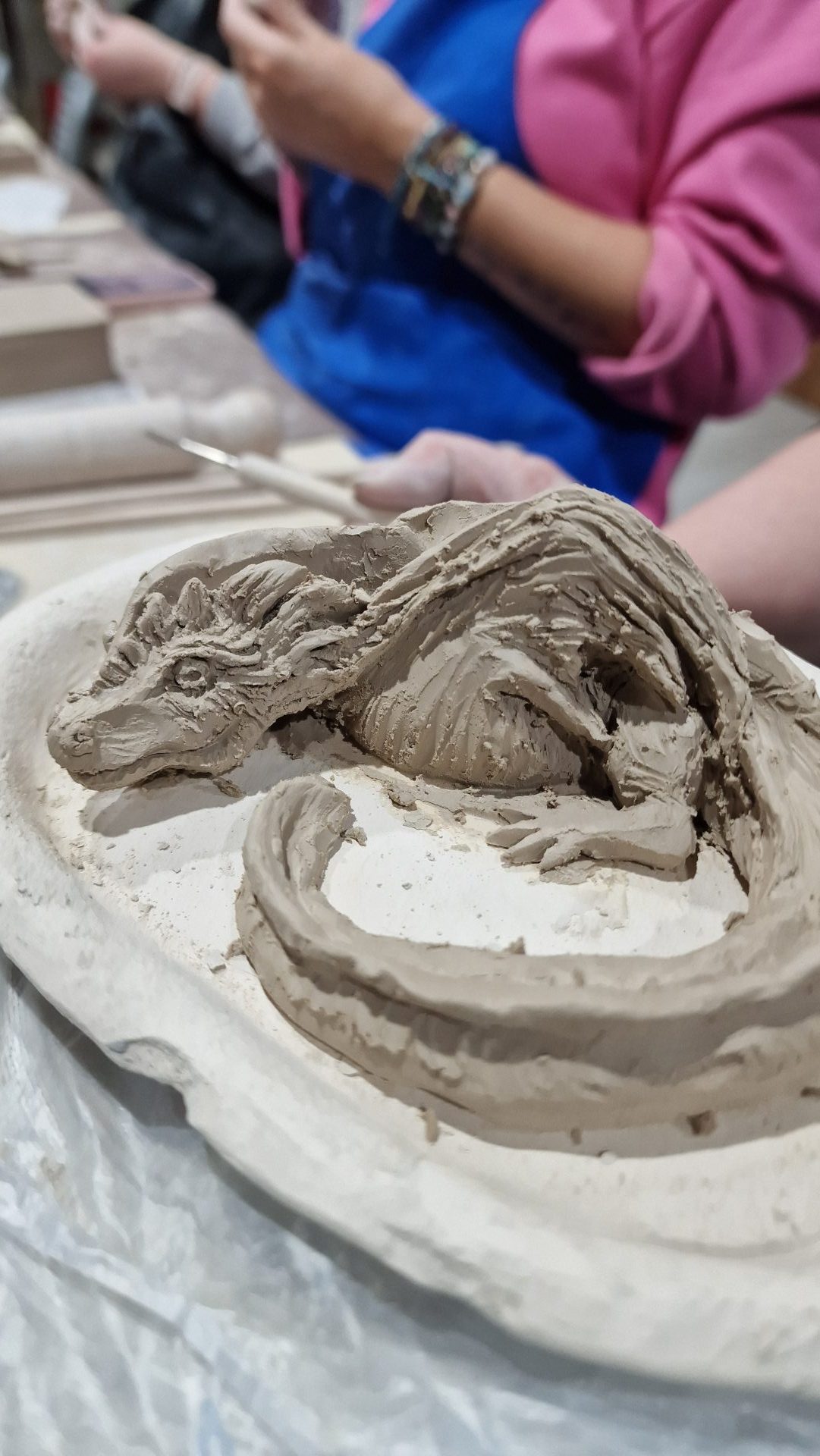 Szczegółowa rzeźba smoka ulepiona z jasnej gliny podczas zajęć ceramicznych dla młodzieży.
